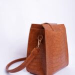Brown textured leather handbag with strap against white backdrop, elegant and timeless accessory.